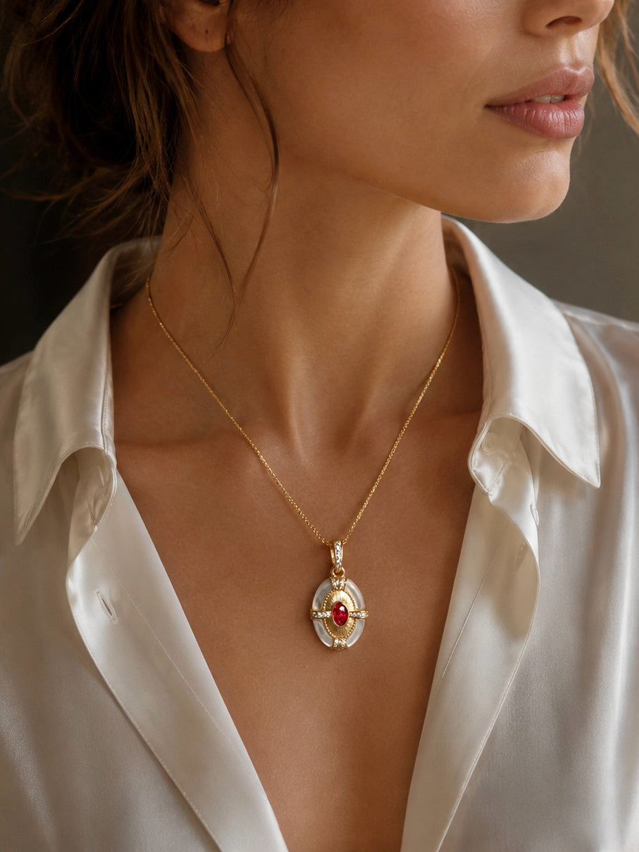 Gold beaded necklace with oval red-and-pearl pendant, worn with a white blouse