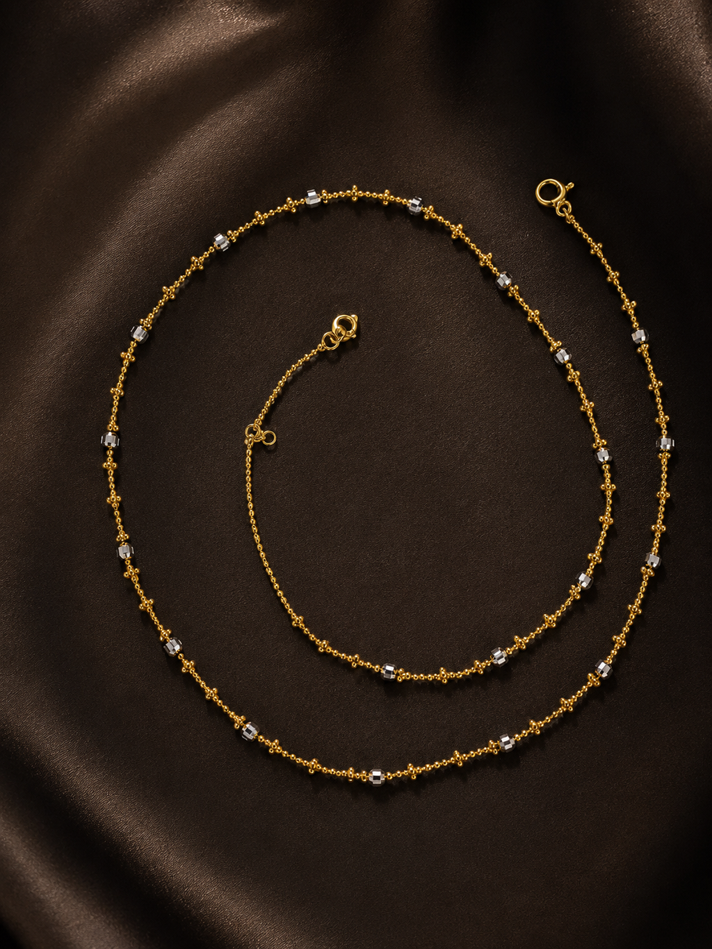 Silver necklace with two beaded chain strands and clasp, laid on dark fabric.