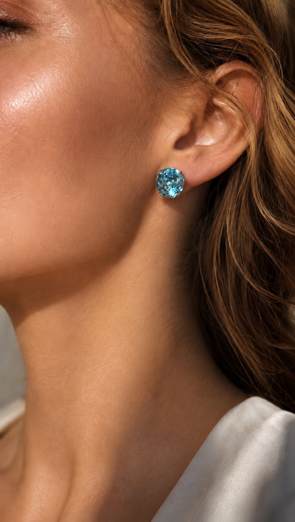 Blue topaz stud earrings on ear, small faceted round gemstone with silver prongs