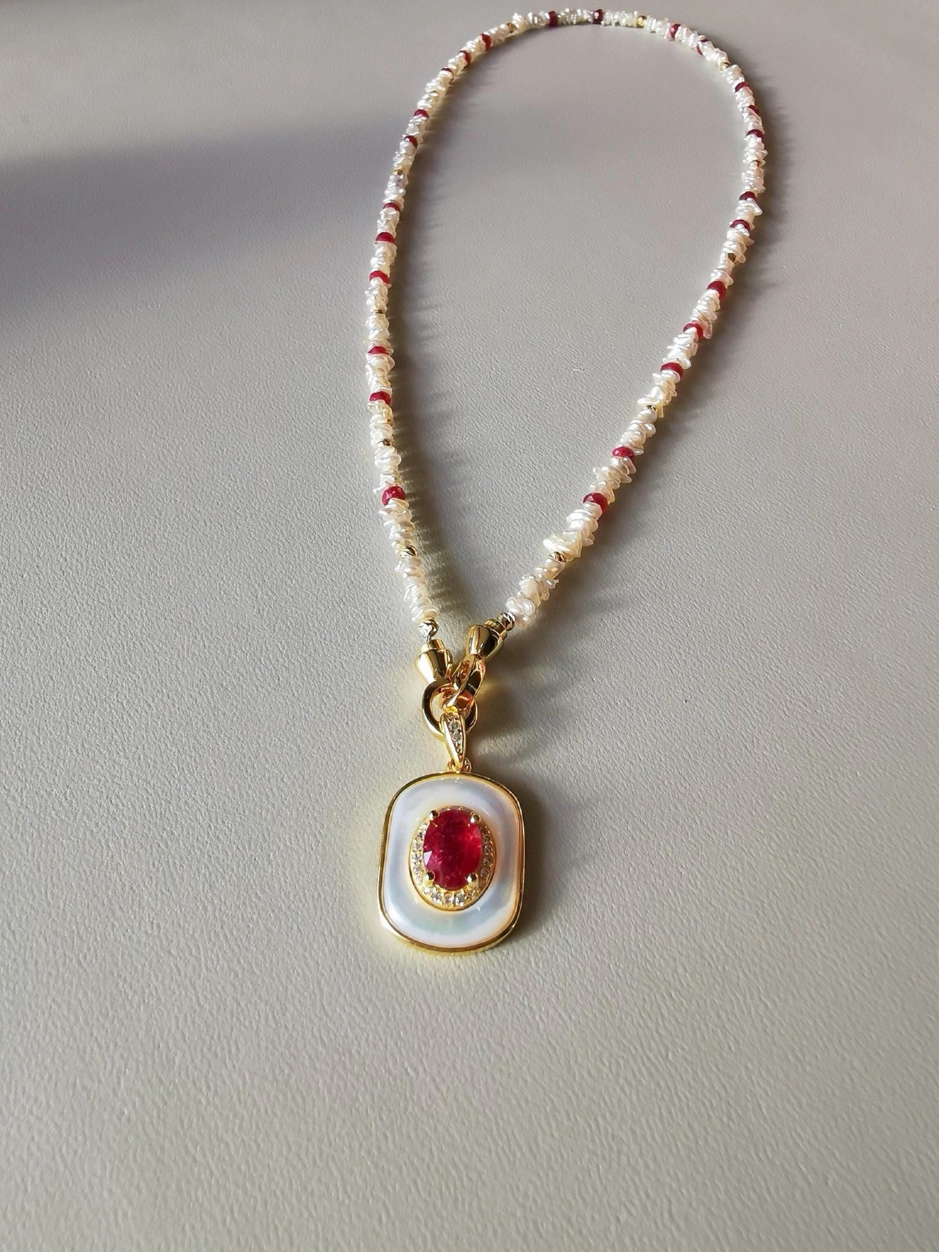 Gold bail ruby and mother-of-pearl pendant with red bead accents on beaded chain