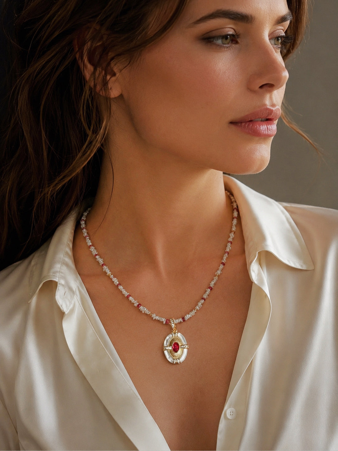 Beaded gold necklace with oval red-and-pearl pendant, worn close to the collar