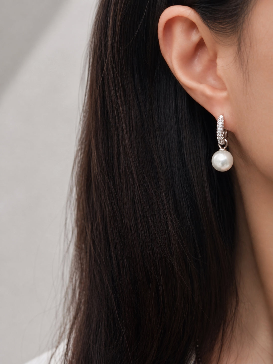 Close-up of silver hoop lock earrings with textured pavé hoops and round pearl drop
