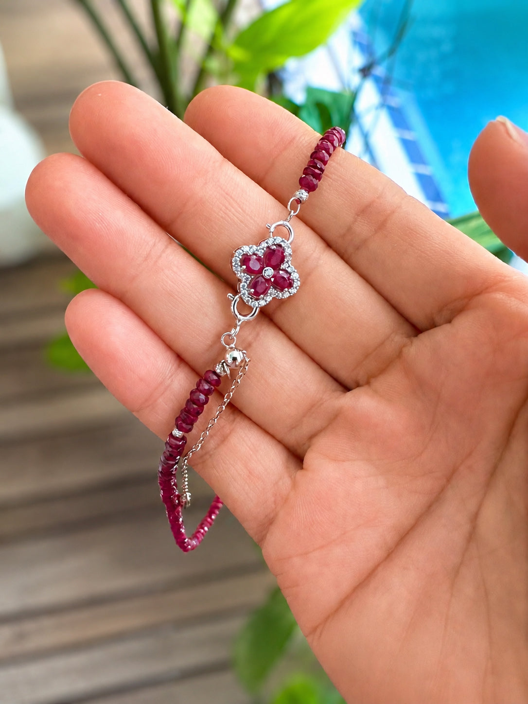 Four-leaf clover pendant charm on a silver chain, shown over a hand