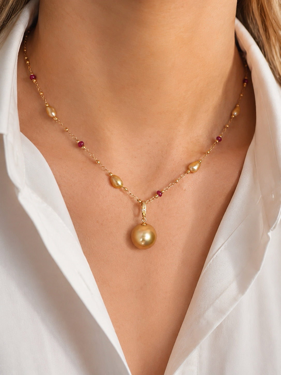 Gold pearl pendant necklace worn on the neck with red gemstone bead accents