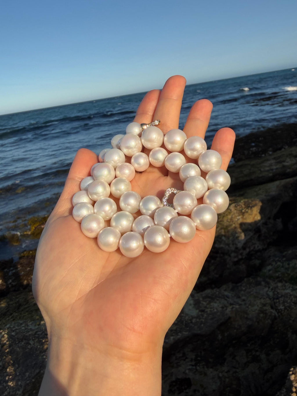 Pearl necklace with round iridescent pearls, shown in a hand