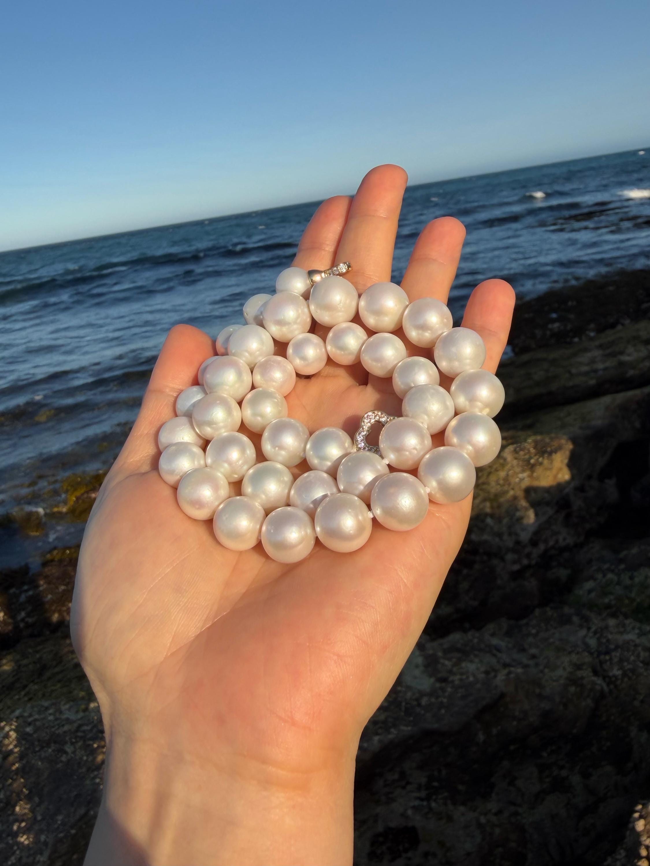 Pearl necklace with round iridescent pearls, shown in a hand