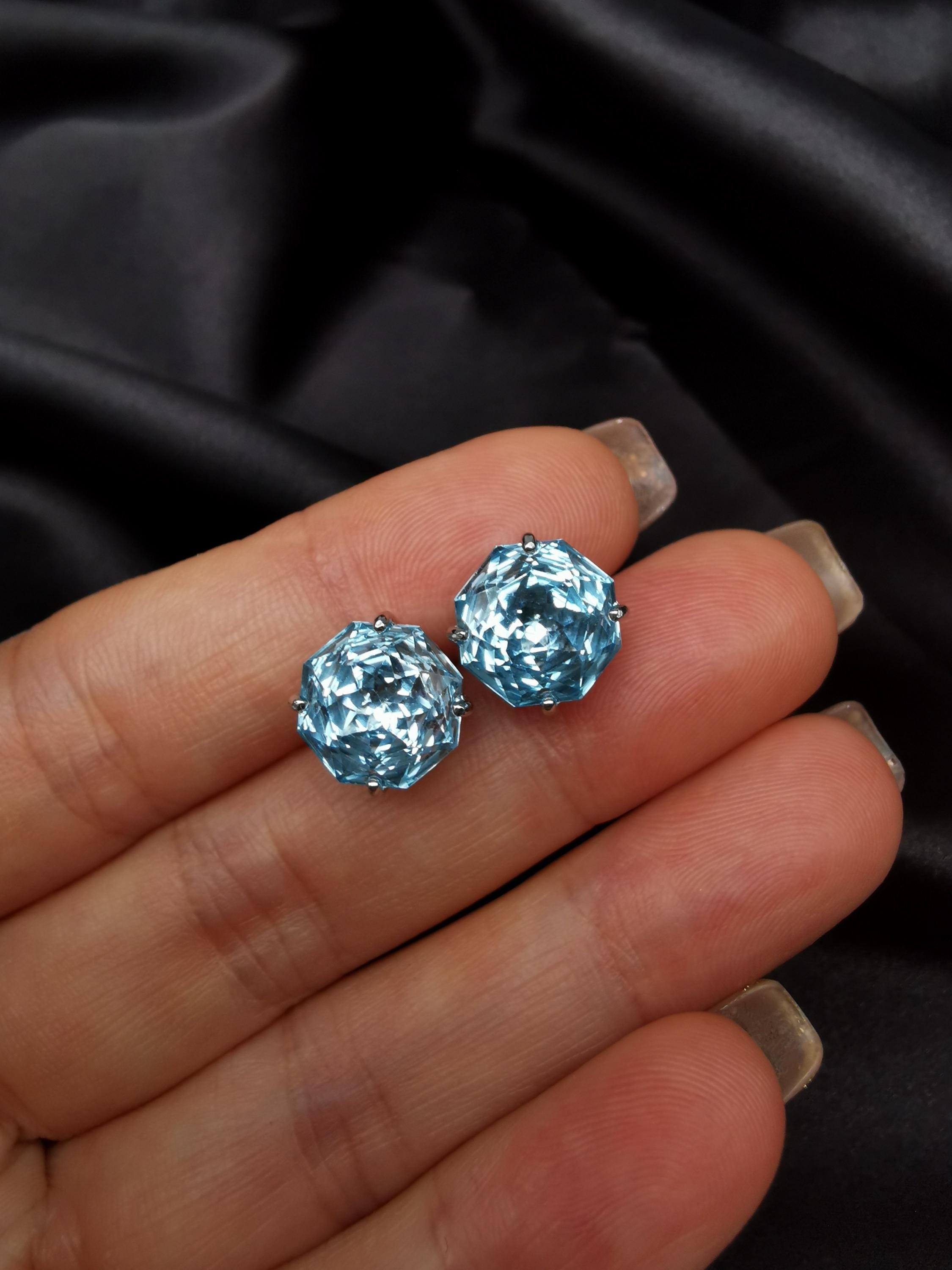 Blue topaz stud earrings close-up on hand, faceted round stones in metal settings