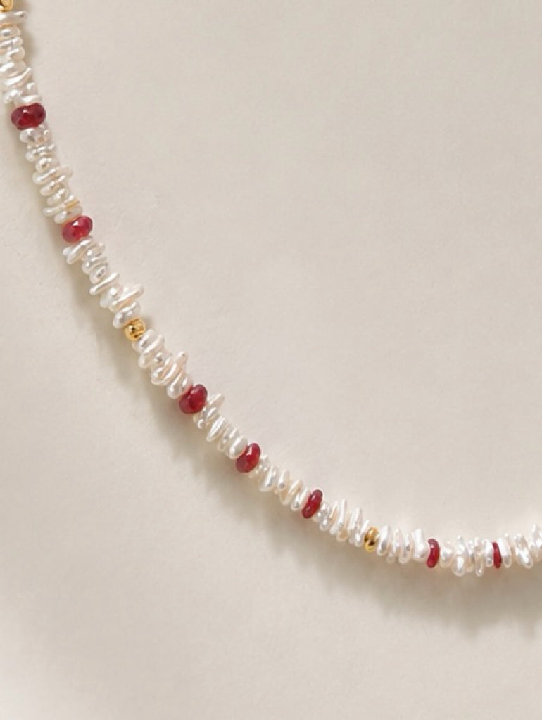 Keshi pearl necklace strand with red ruby bead accents against a light background