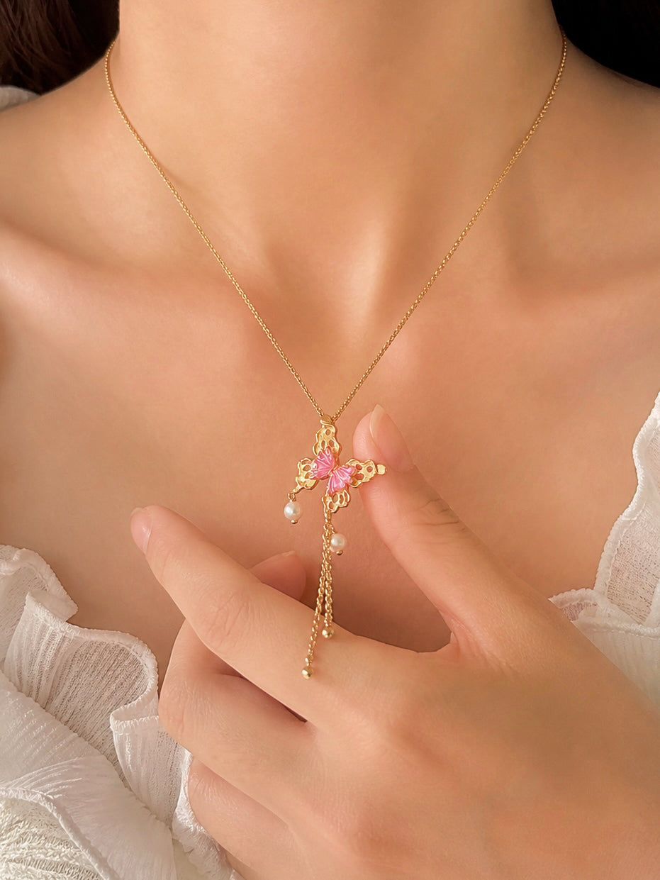 Gold butterfly pendant with pink tourmaline and pearl tassel, held near the collar