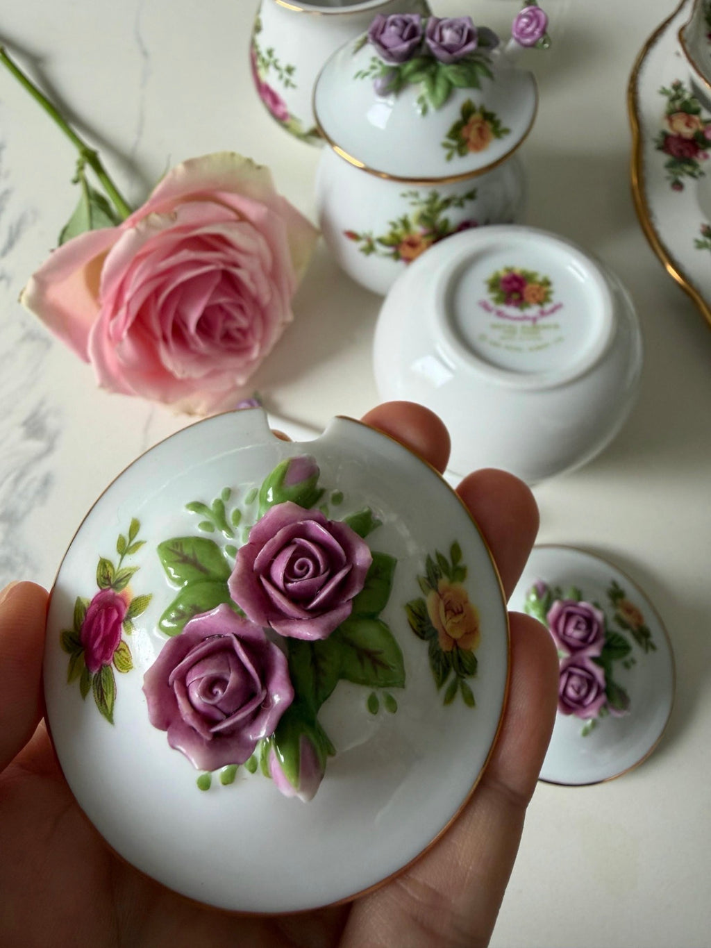 Porcelain jar lid held in hand with purple rose floral pattern and gold rim
