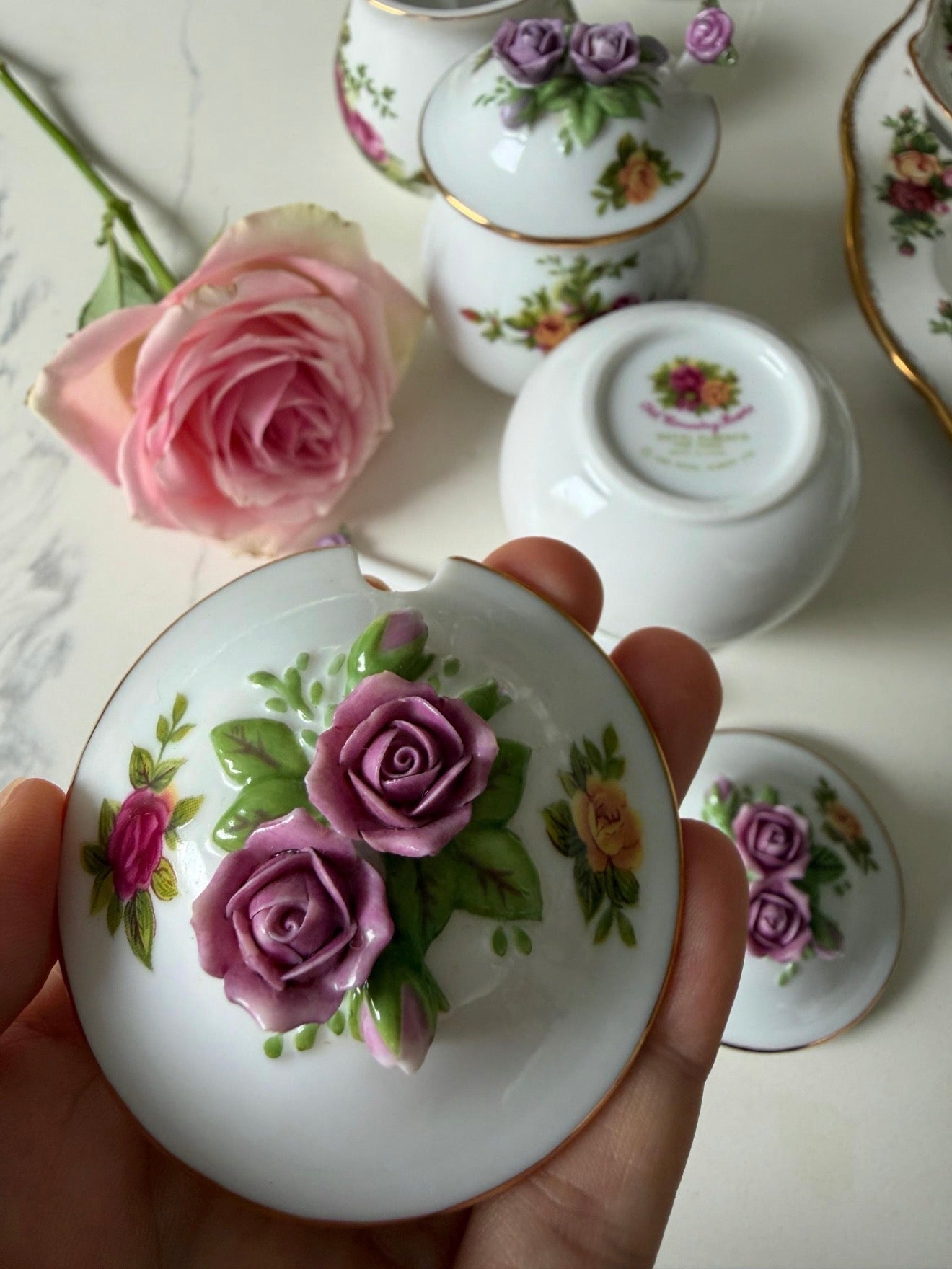 Porcelain jar lid held in hand with purple rose floral pattern and gold rim