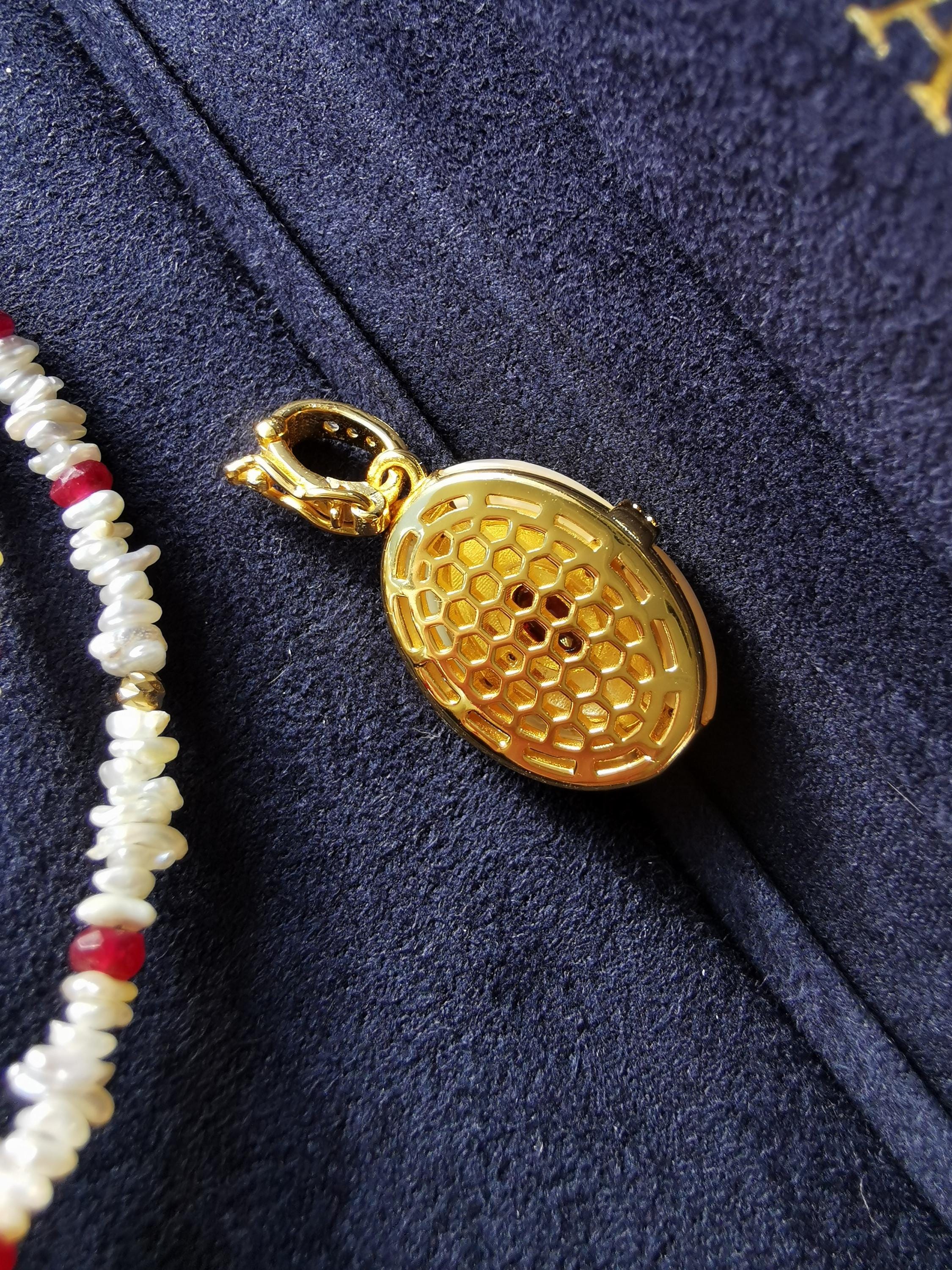 Gold oval pendant charm with honeycomb texture, beside clasp and bead strands