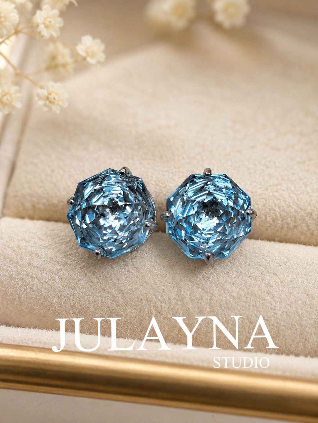 Blue topaz stud earrings on beige fabric, faceted round stones in silver bezel settings