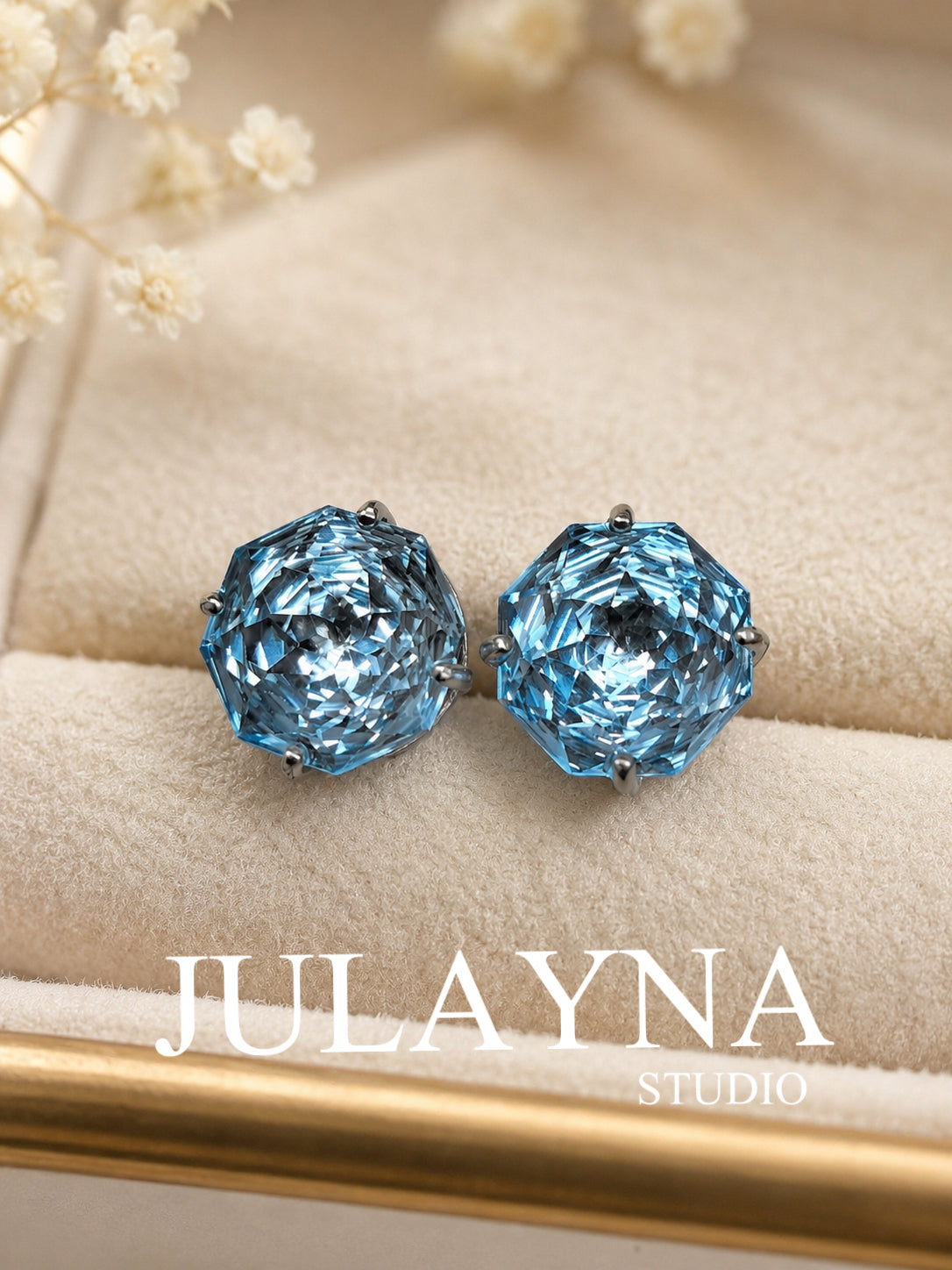 Blue topaz stud earrings on beige fabric, faceted round stones in silver bezel settings