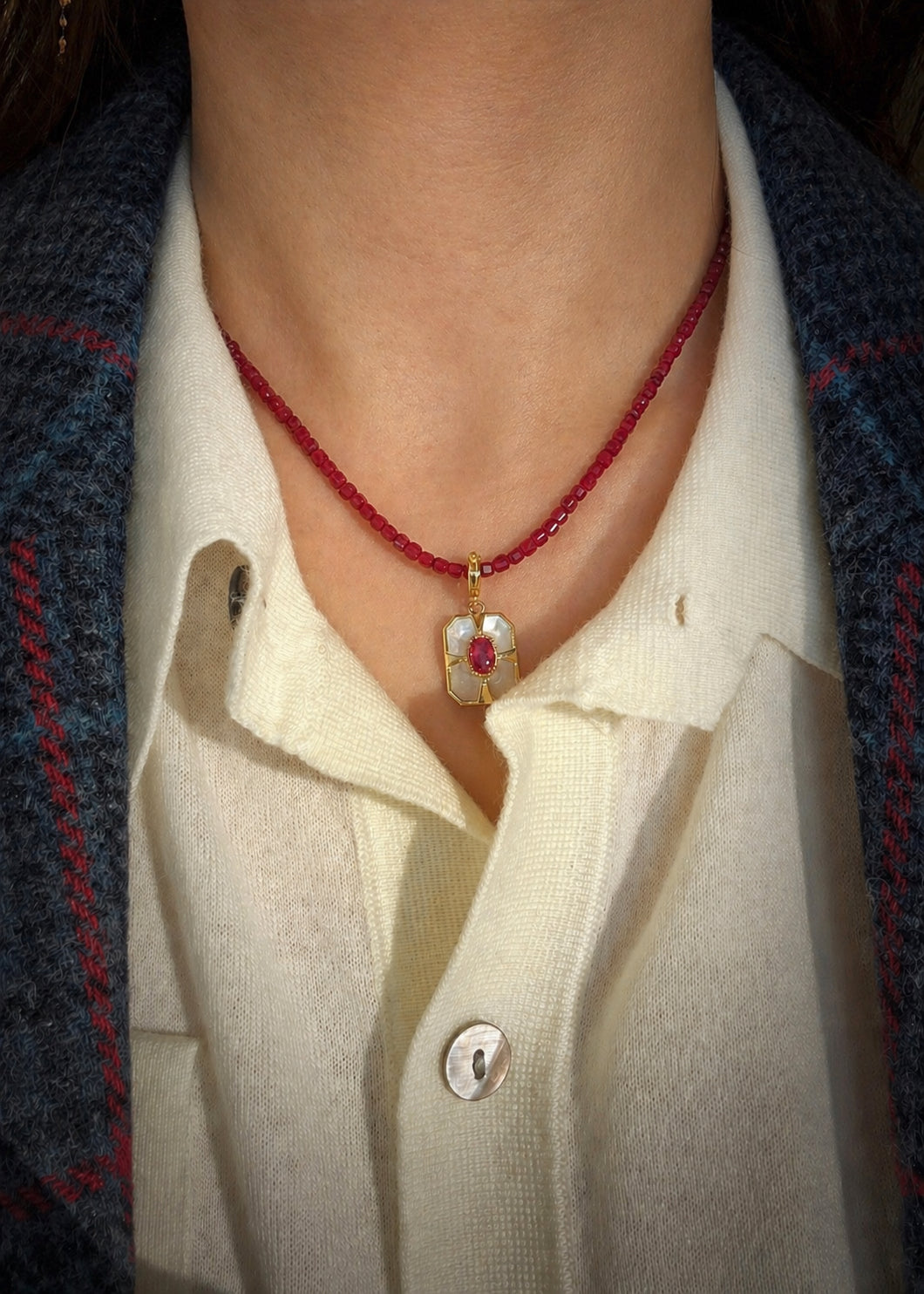 Ruby bead necklace with small dangling charm and gold-tone clasp on neckline