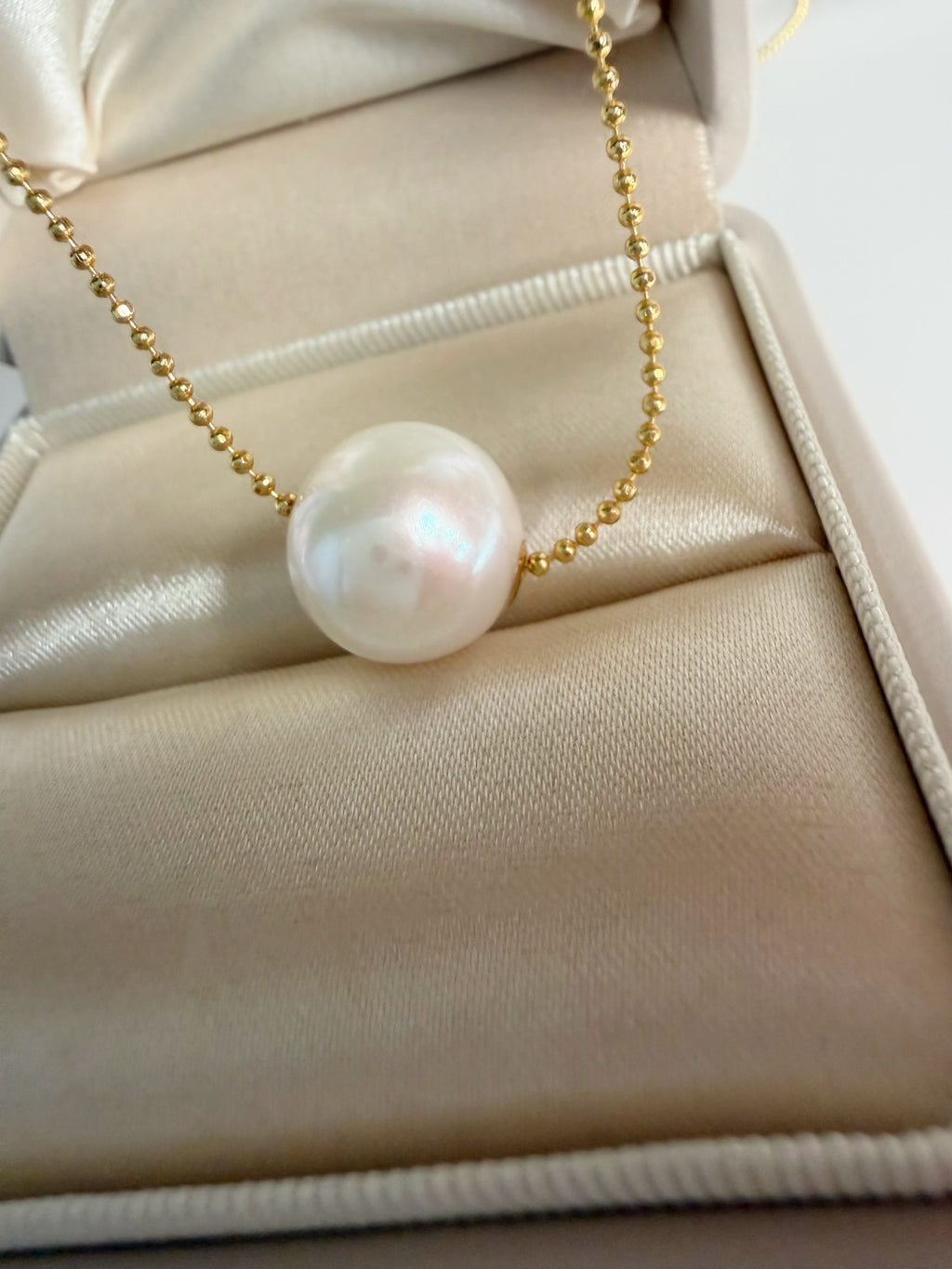 Gold-tone chain necklace with white freshwater pearl pendant, close-up