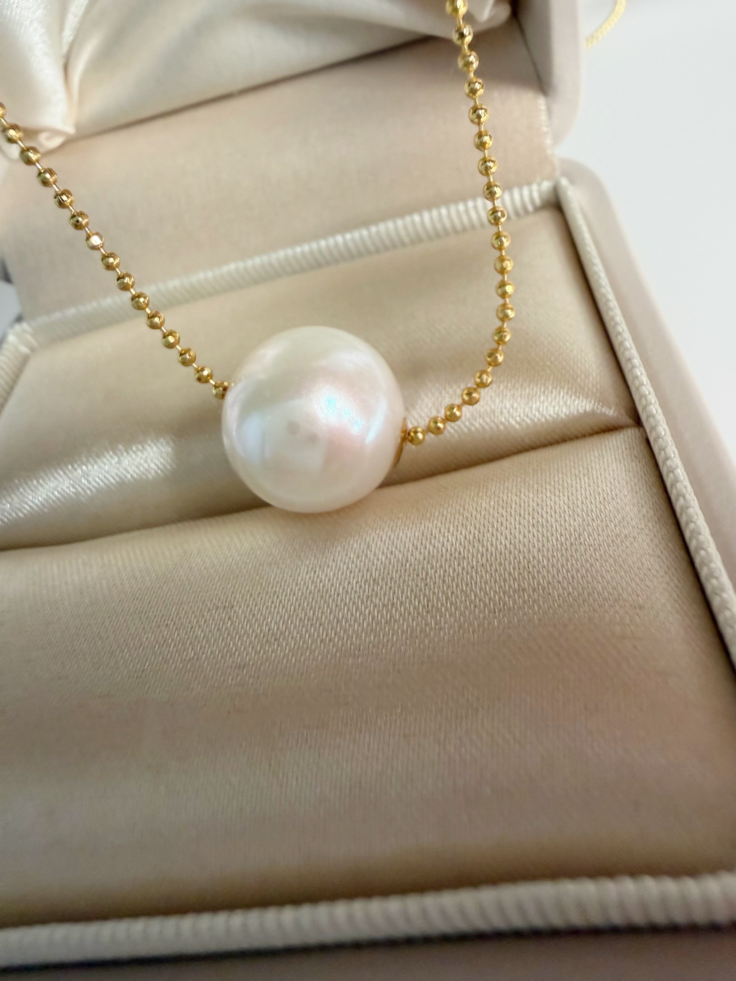 Gold-tone chain necklace with white freshwater pearl pendant, close-up