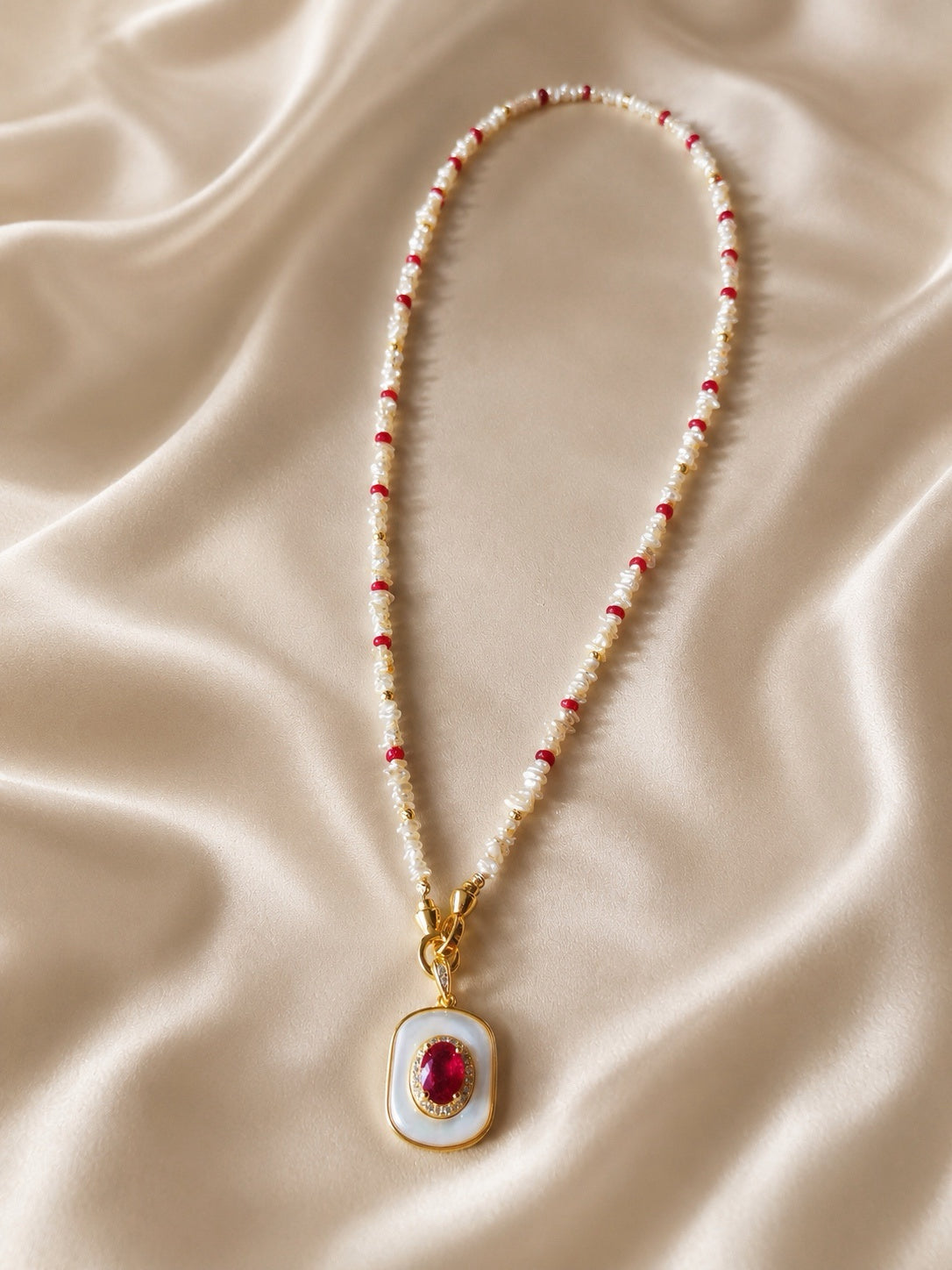 Beaded necklace with red and white beads and a gold-tone mother-of-pearl ruby pendant