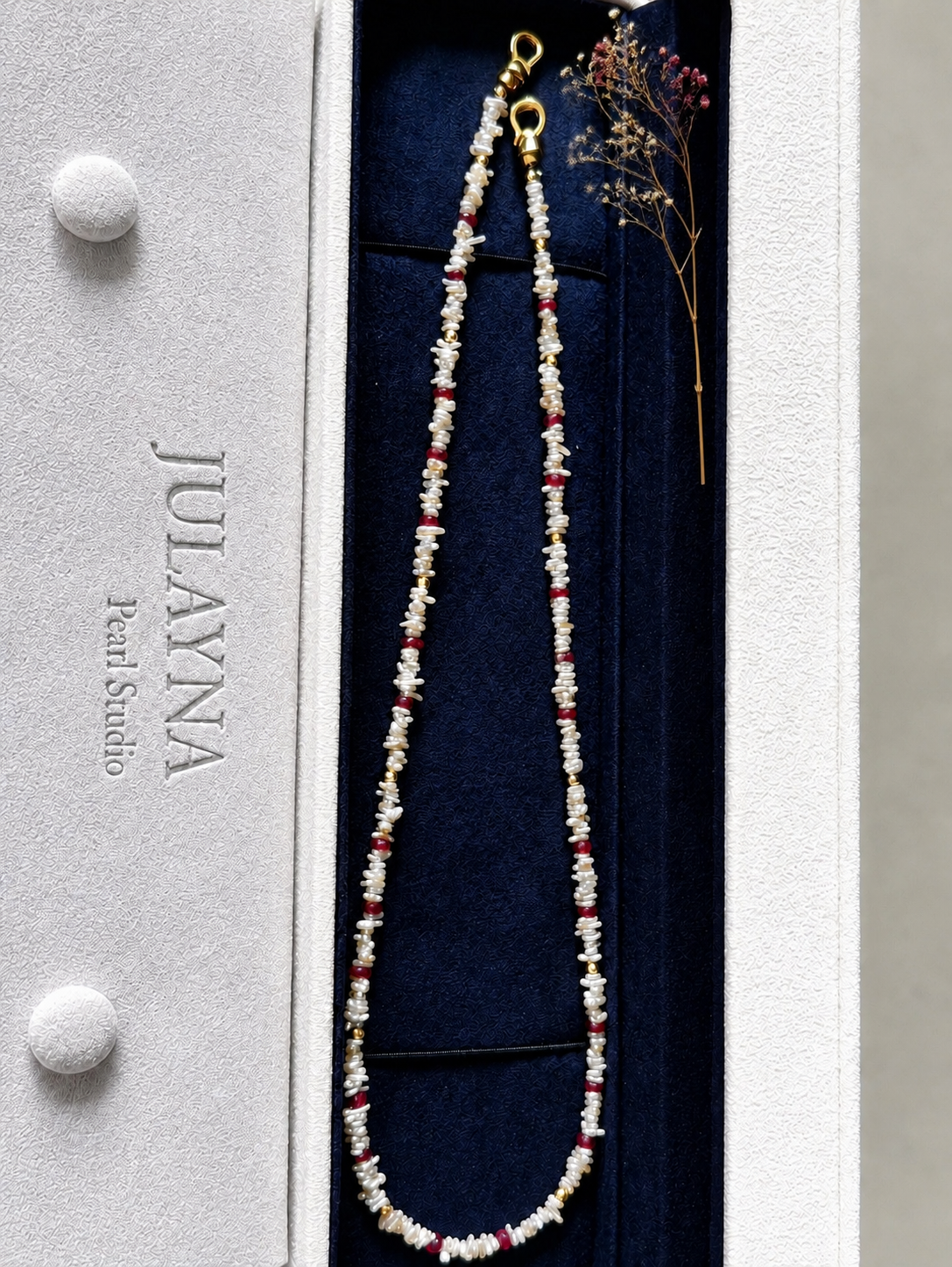 Keshi pearl necklace with red ruby accents displayed on a navy jewelry card