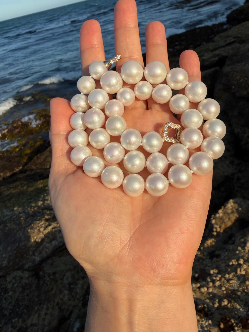 Pearl necklace with round iridescent pearls and a gold-tone clasp, held up