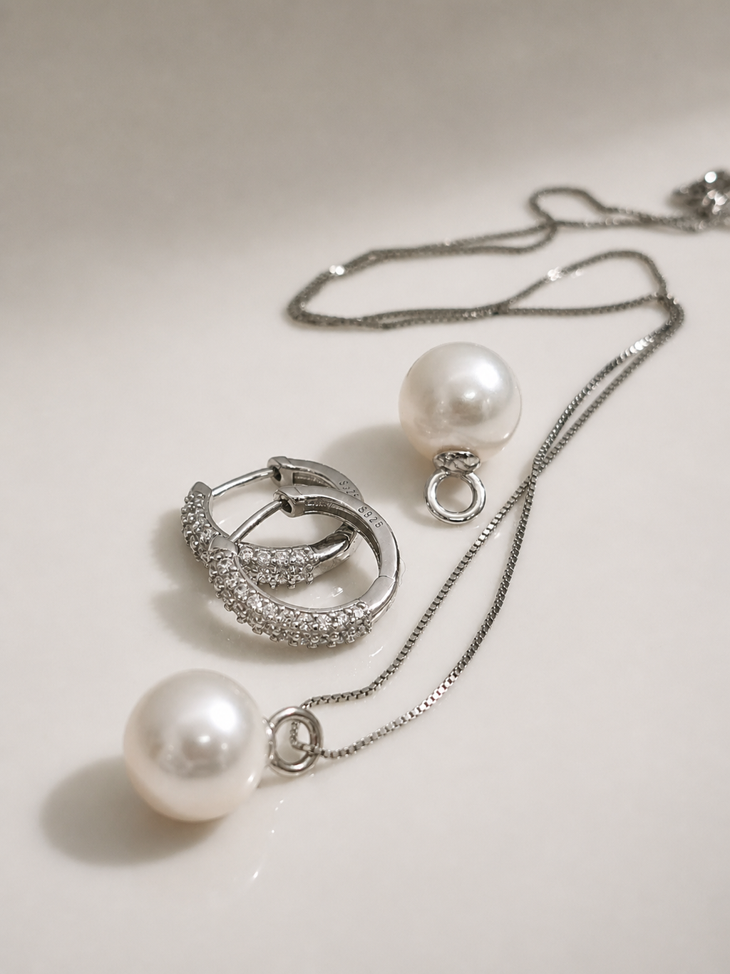 Silver hoop lock earrings with pearl drops and textured hoops, jewelry pieces laid flat