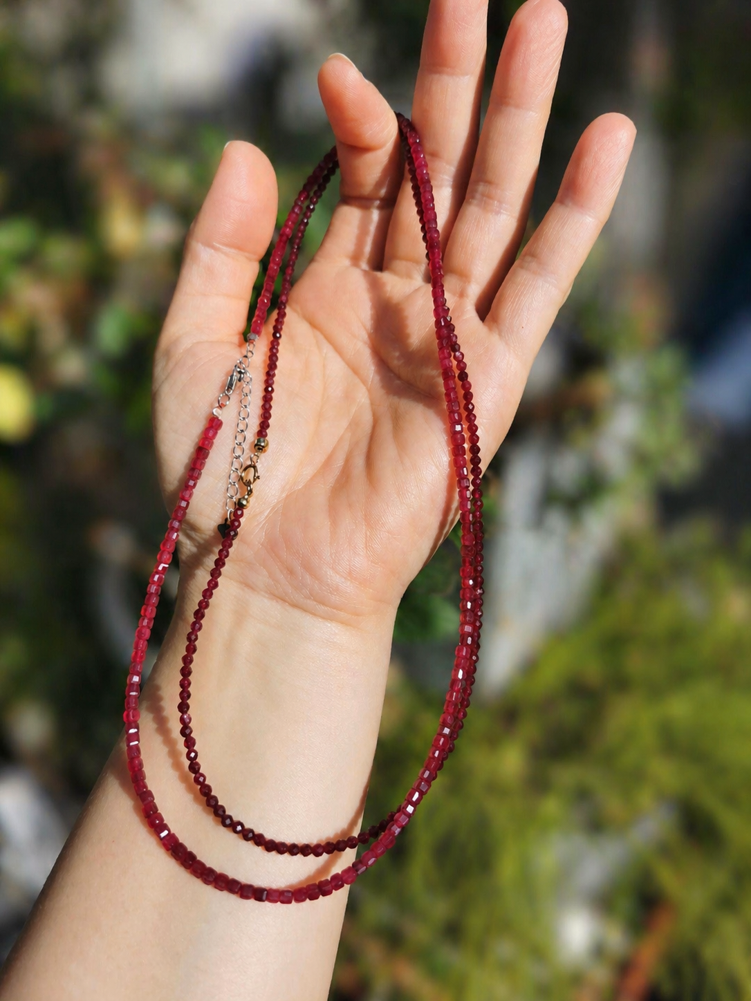 Ruby square-cut bead necklace with silver-toned connectors, laid across open palm