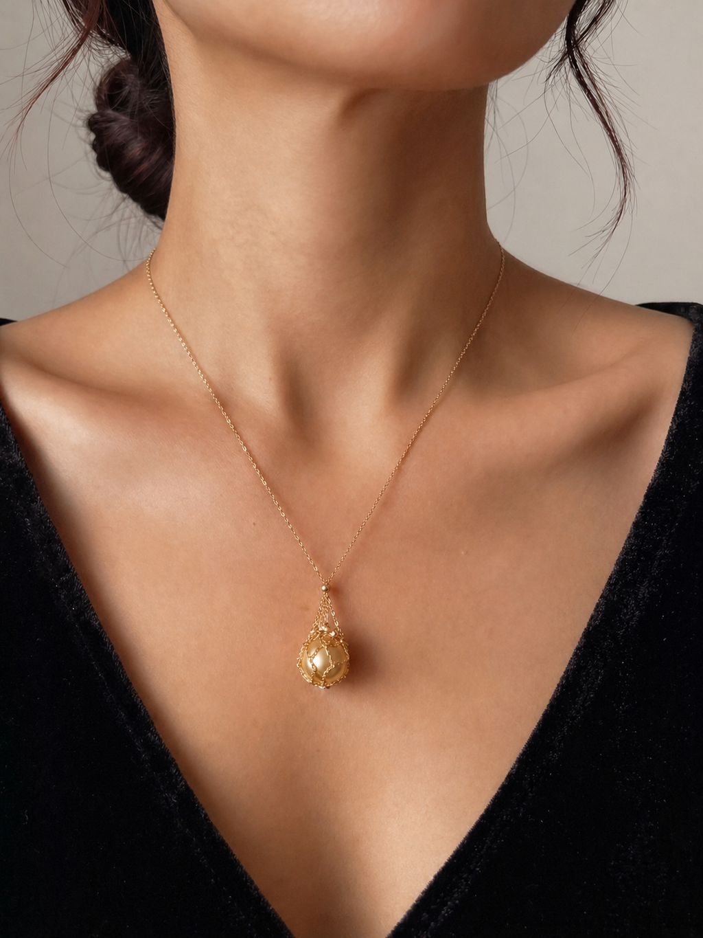Gold tone teardrop net pendant necklace worn with golden pearl bead charm