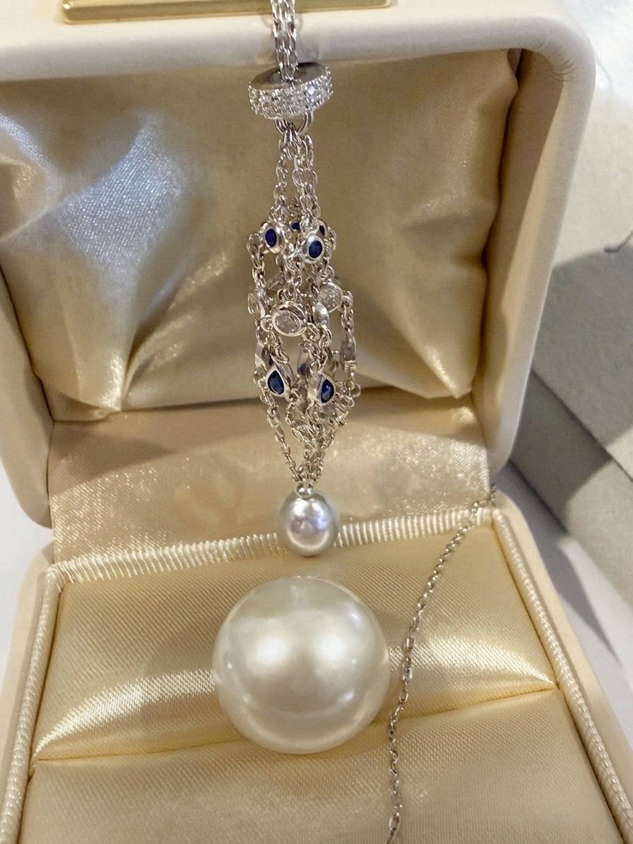 Openwork teardrop pendant necklace with blue stones and round pearl drop, shown on jewelry tray