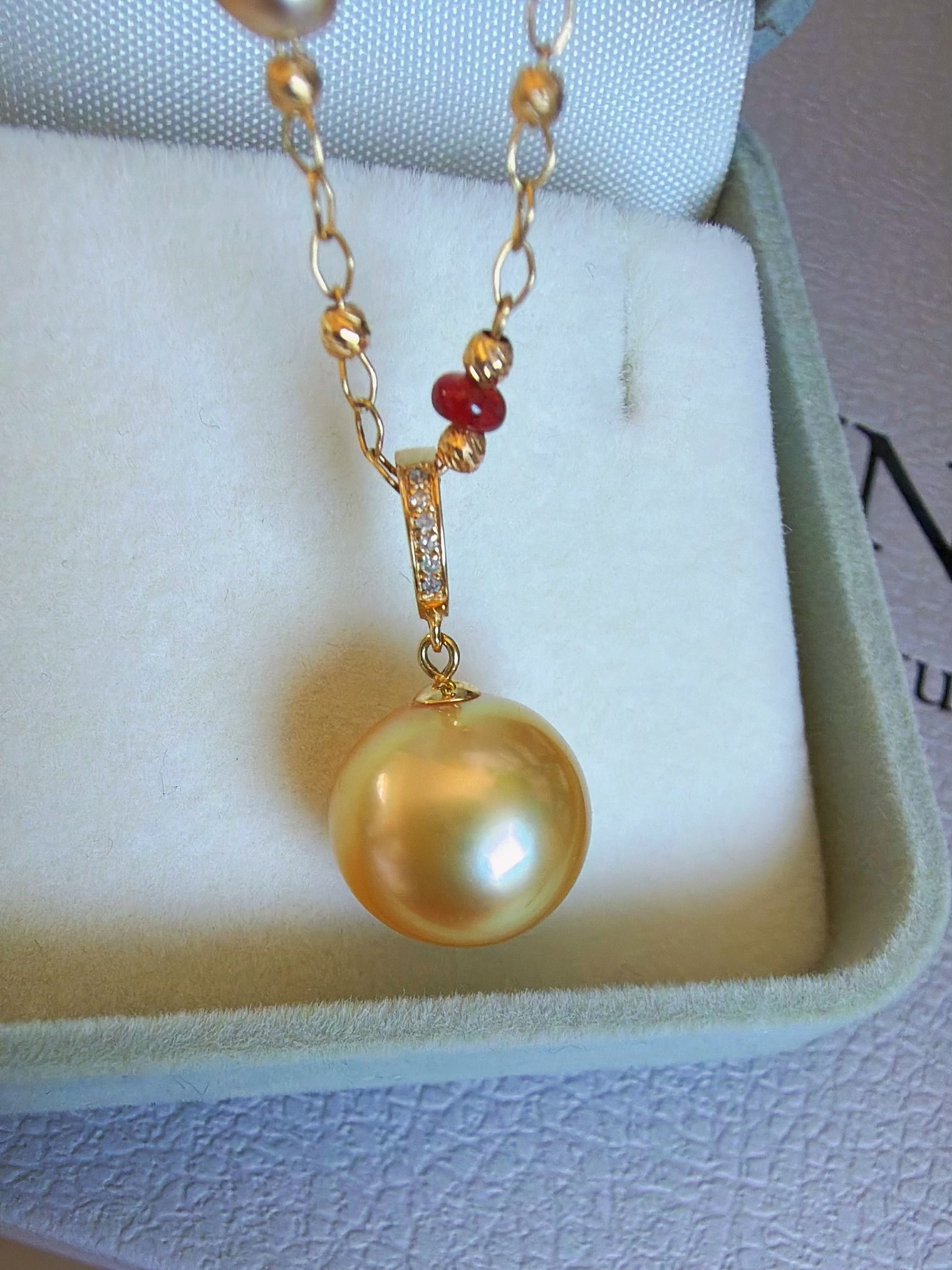 Gold pearl pendant necklace displayed in a jewelry box with red bead details