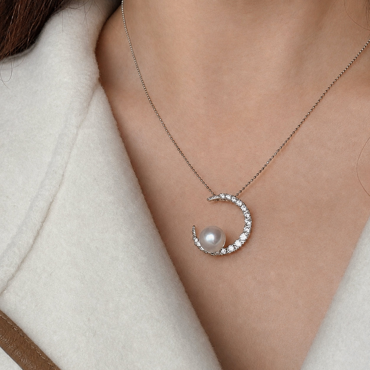 Silver crescent pearl pendant shown on a necklace chain at neckline