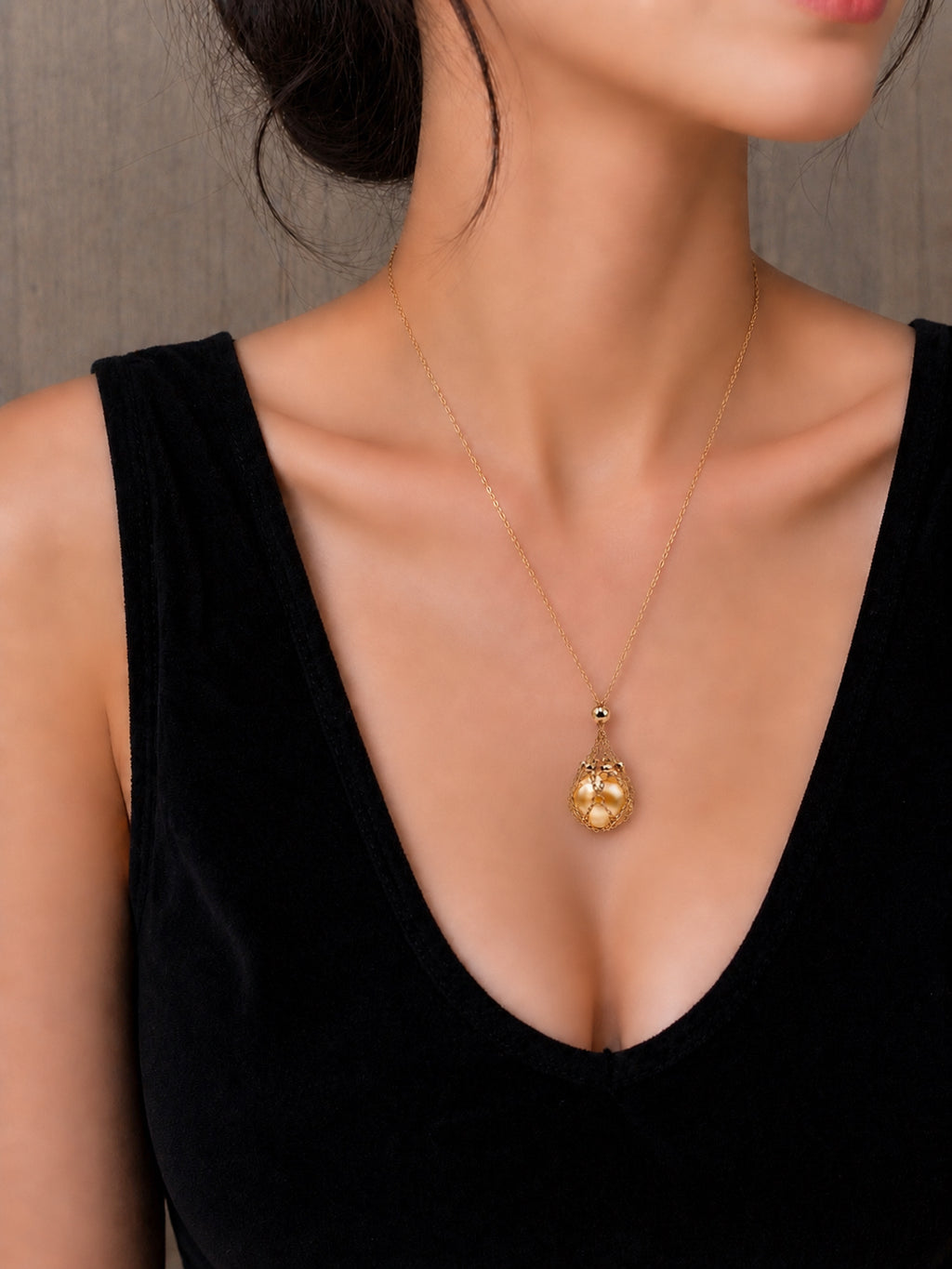 Gold-toned pendant necklace with teardrop net charm at the center of the chest