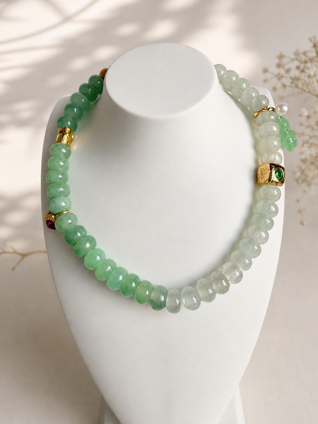 Jadeite beaded bracelet with green and white beads and gold charms on a white stand