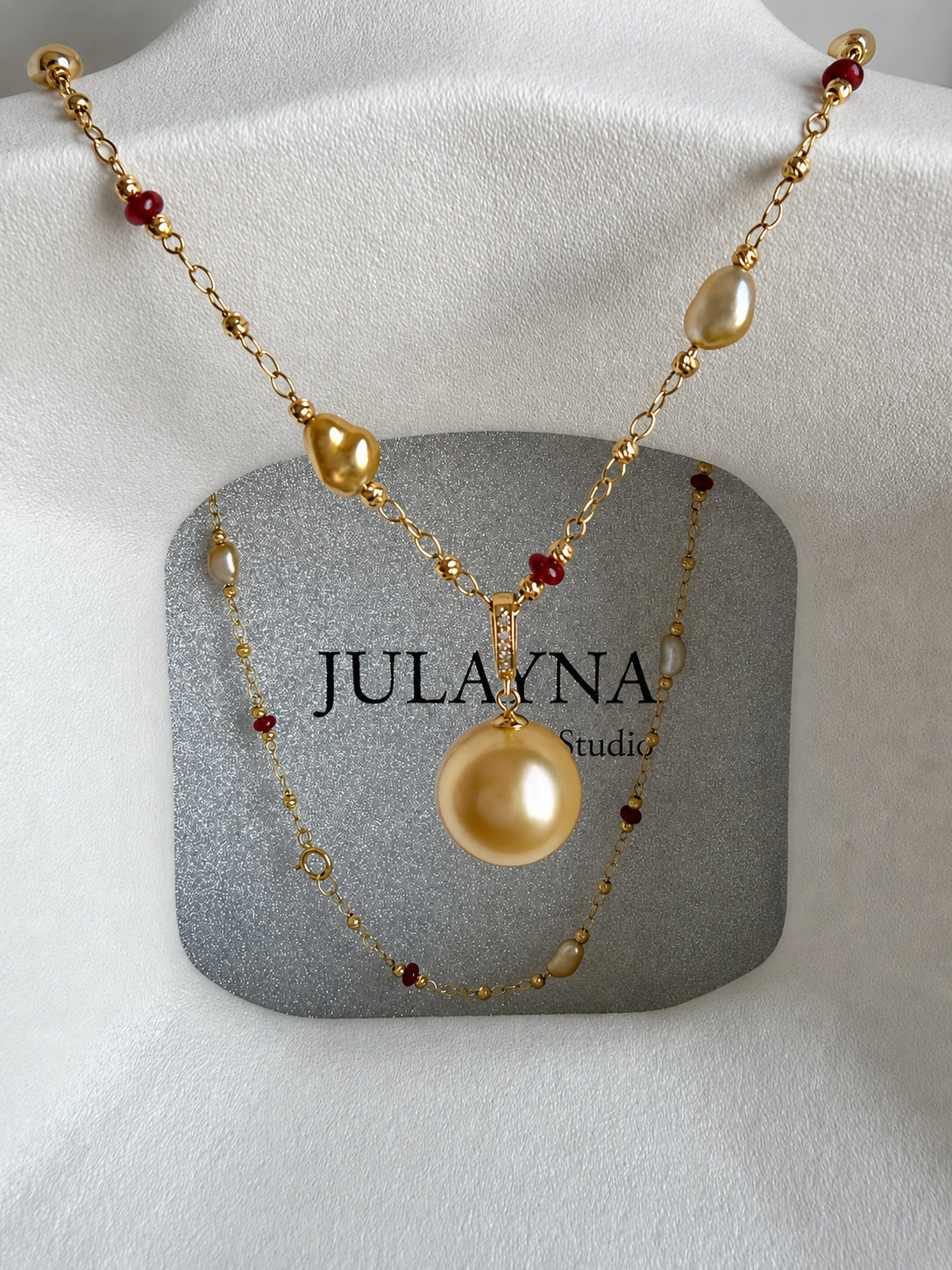 Gold pearl pendant necklace with layered chains and small red gemstone bead accents