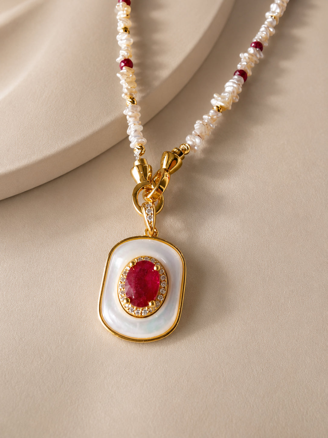 Gold-tone pendant necklace with mother-of-pearl oval frame and ruby center stone