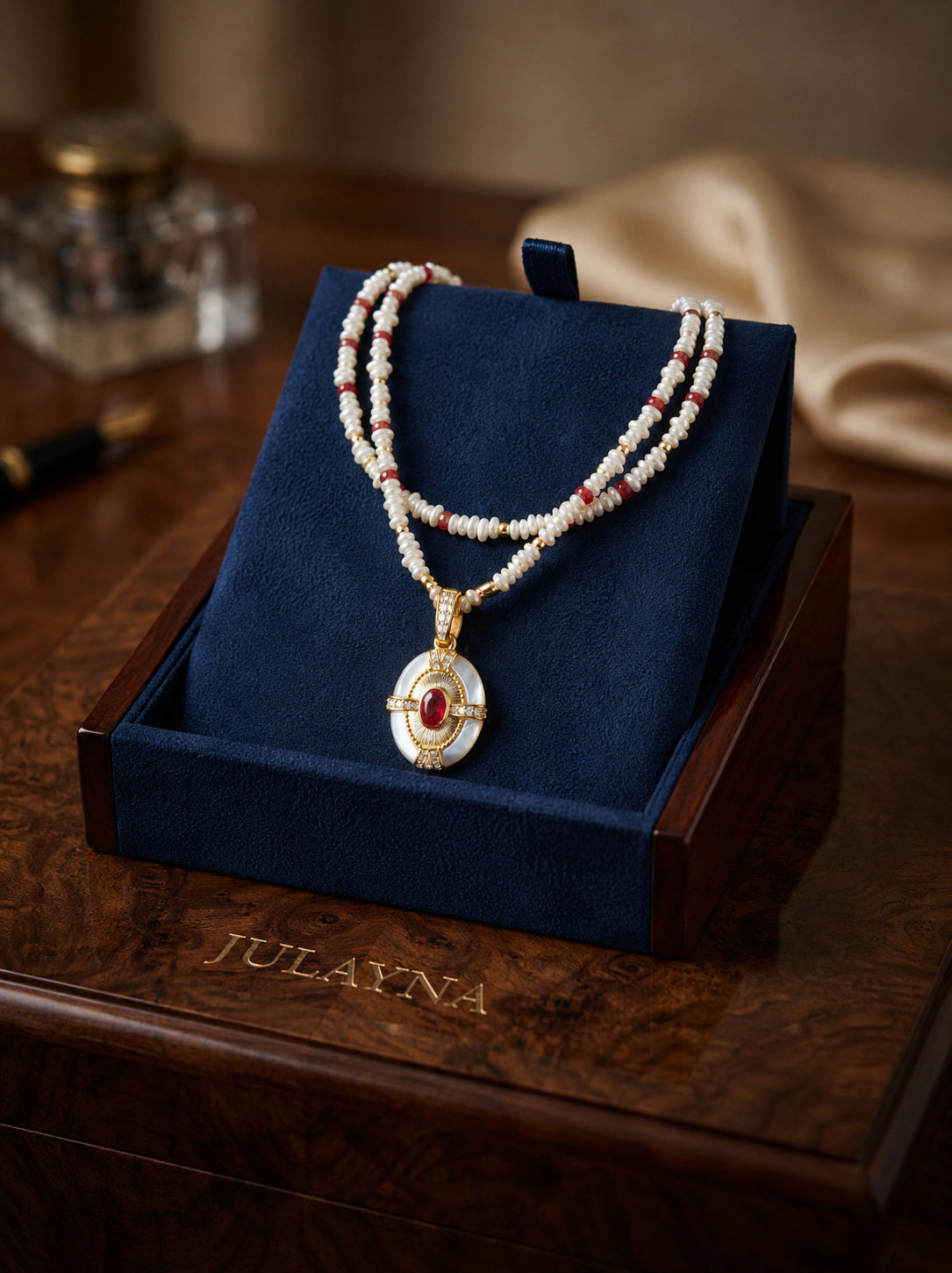 Beaded necklace with gold oval pendant and red center stone on blue jewelry stand