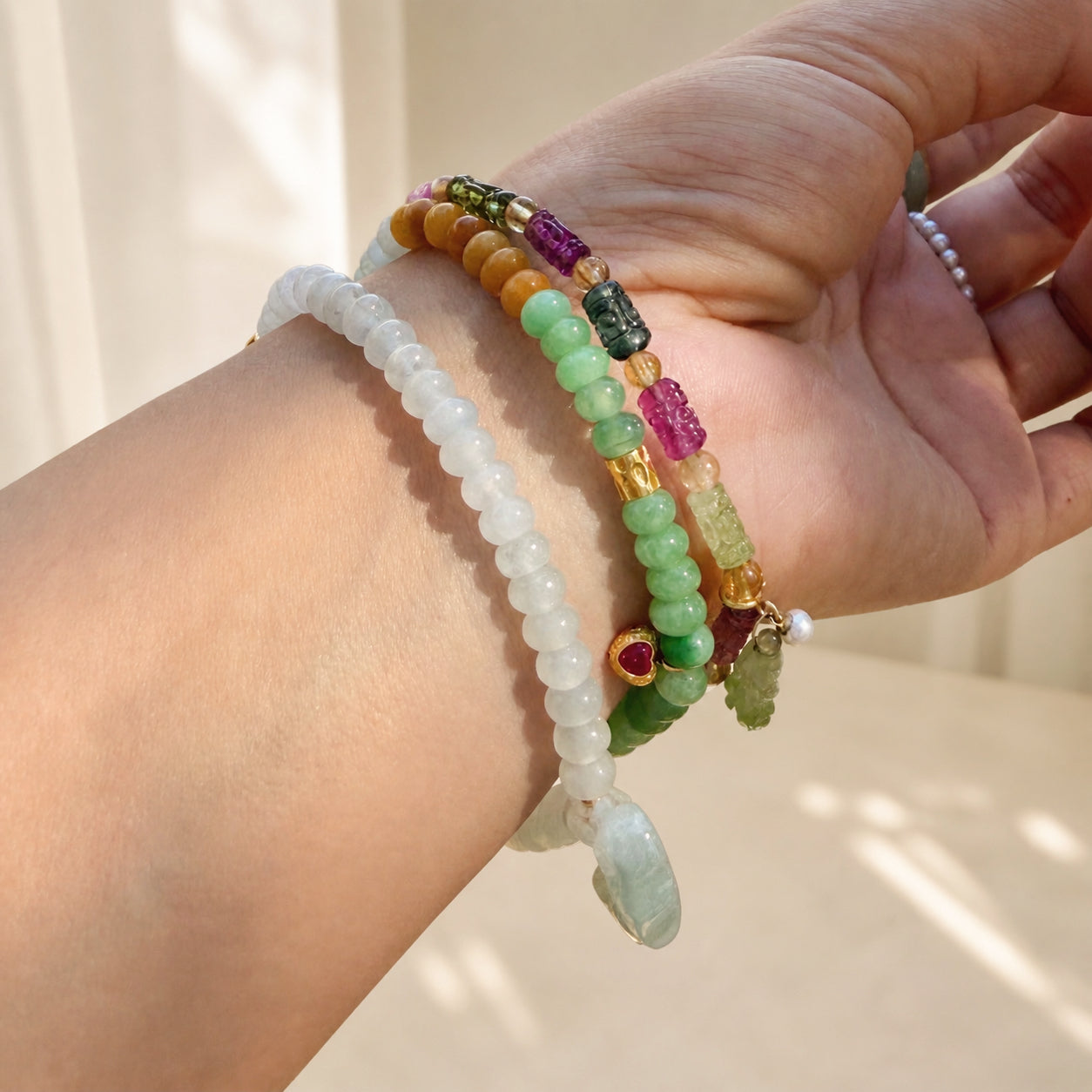 Stacked jadeite bracelets with white, green, and gold charms, plus purple red gemstone details