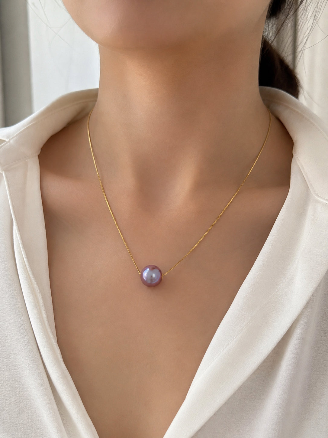 Gold chain necklace with purple round pearl pendant against neckline