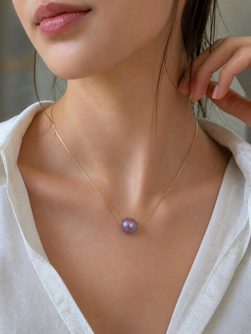 Gold necklace with purple round pearl pendant resting on collarbone