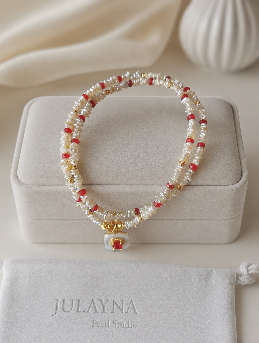 Gold keshi pearl necklace with ruby red accents and round ruby pendant on jewelry box