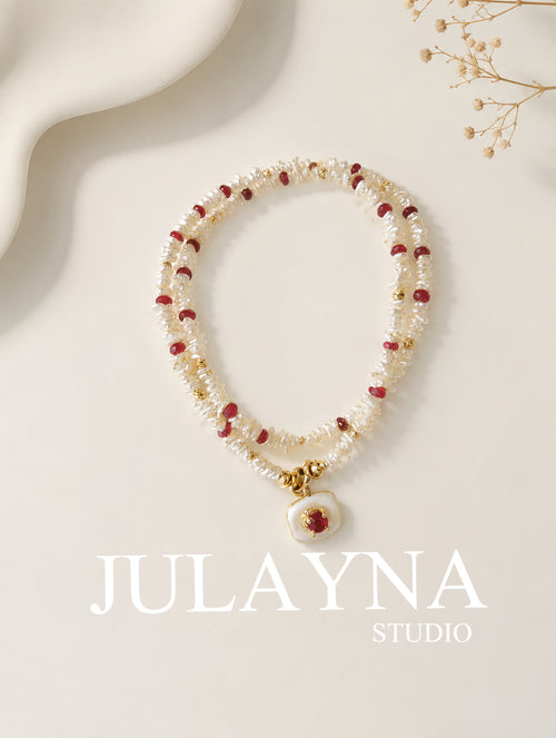 Keshi pearl necklace with red ruby beads and gold clasp, laid on a display card