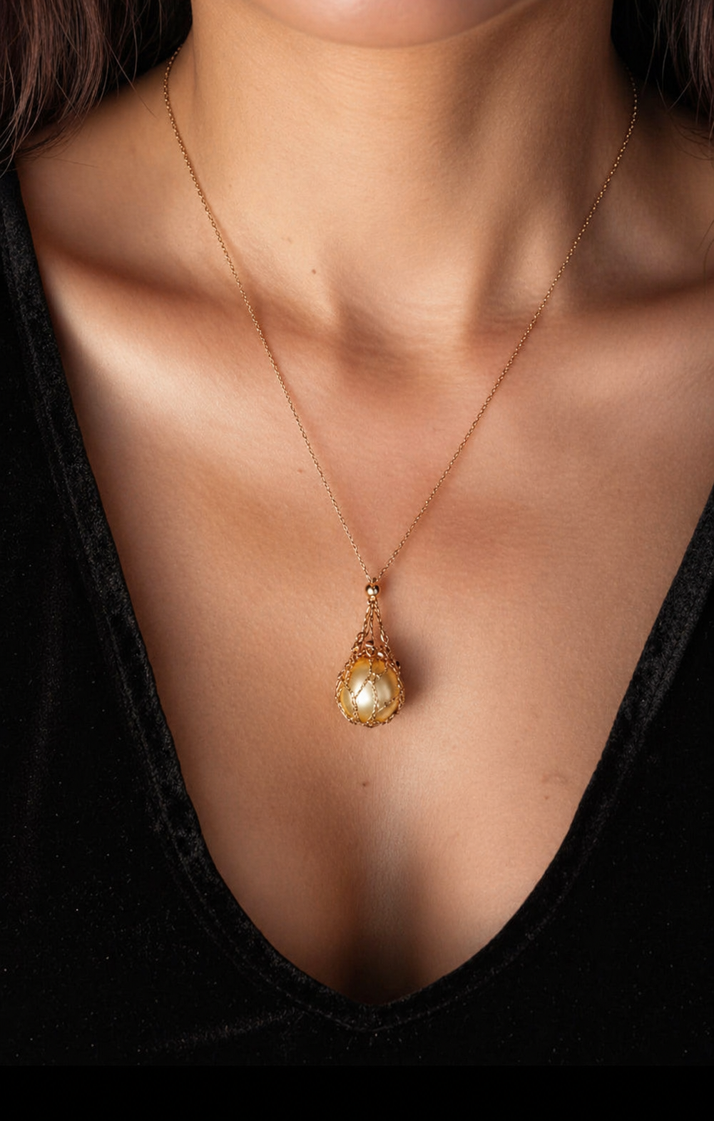 Gold tone net pendant necklace worn on neckline with teardrop charm and golden pearl