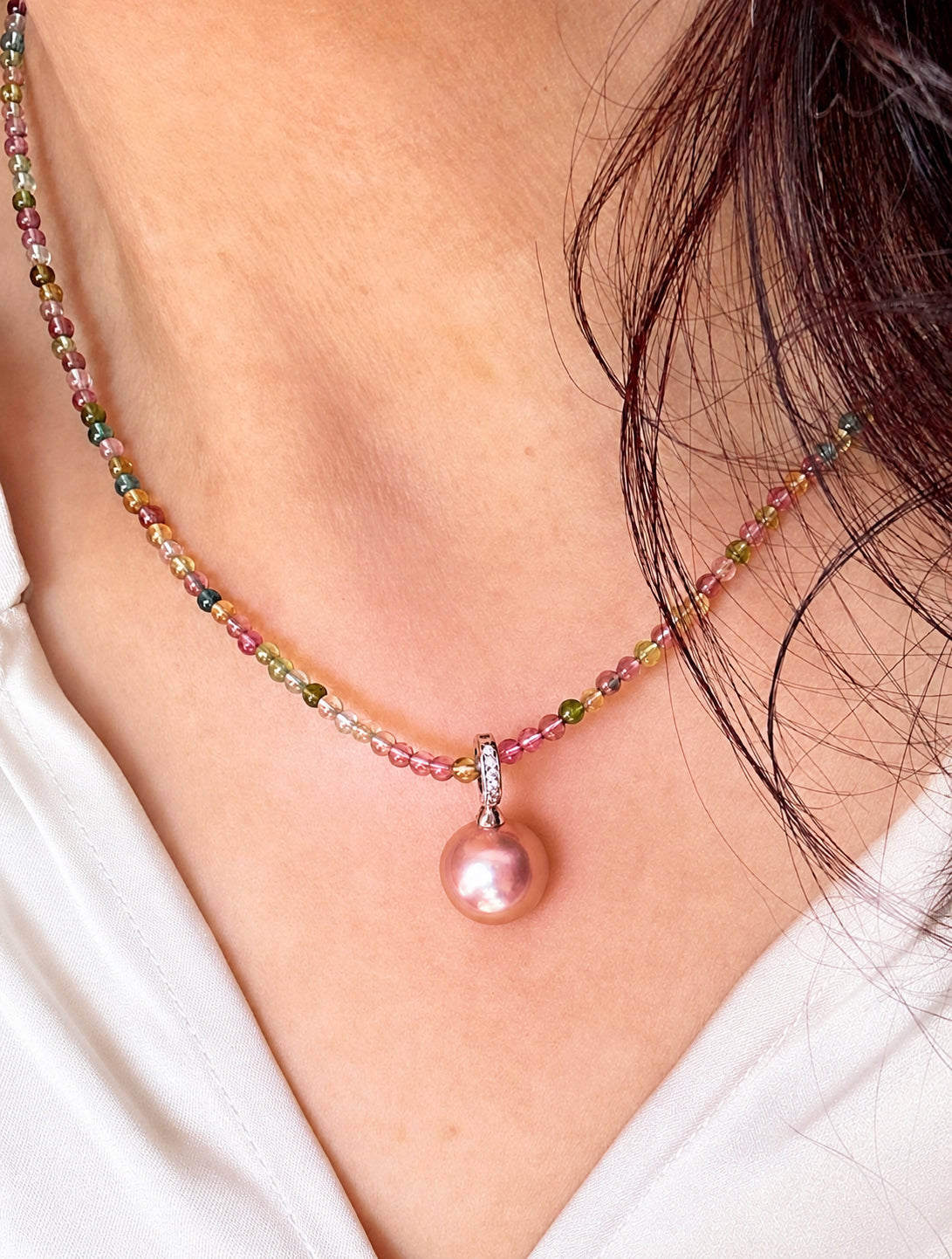 Rainbow bead necklace with rose-pink pearl drop pendant on a white blouse