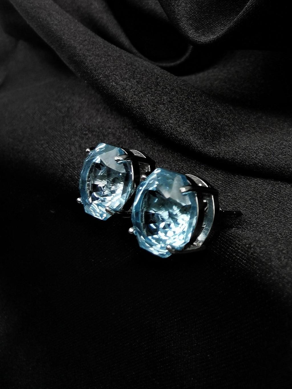 Blue topaz stud earrings close-up, faceted round stones with dark metal accents