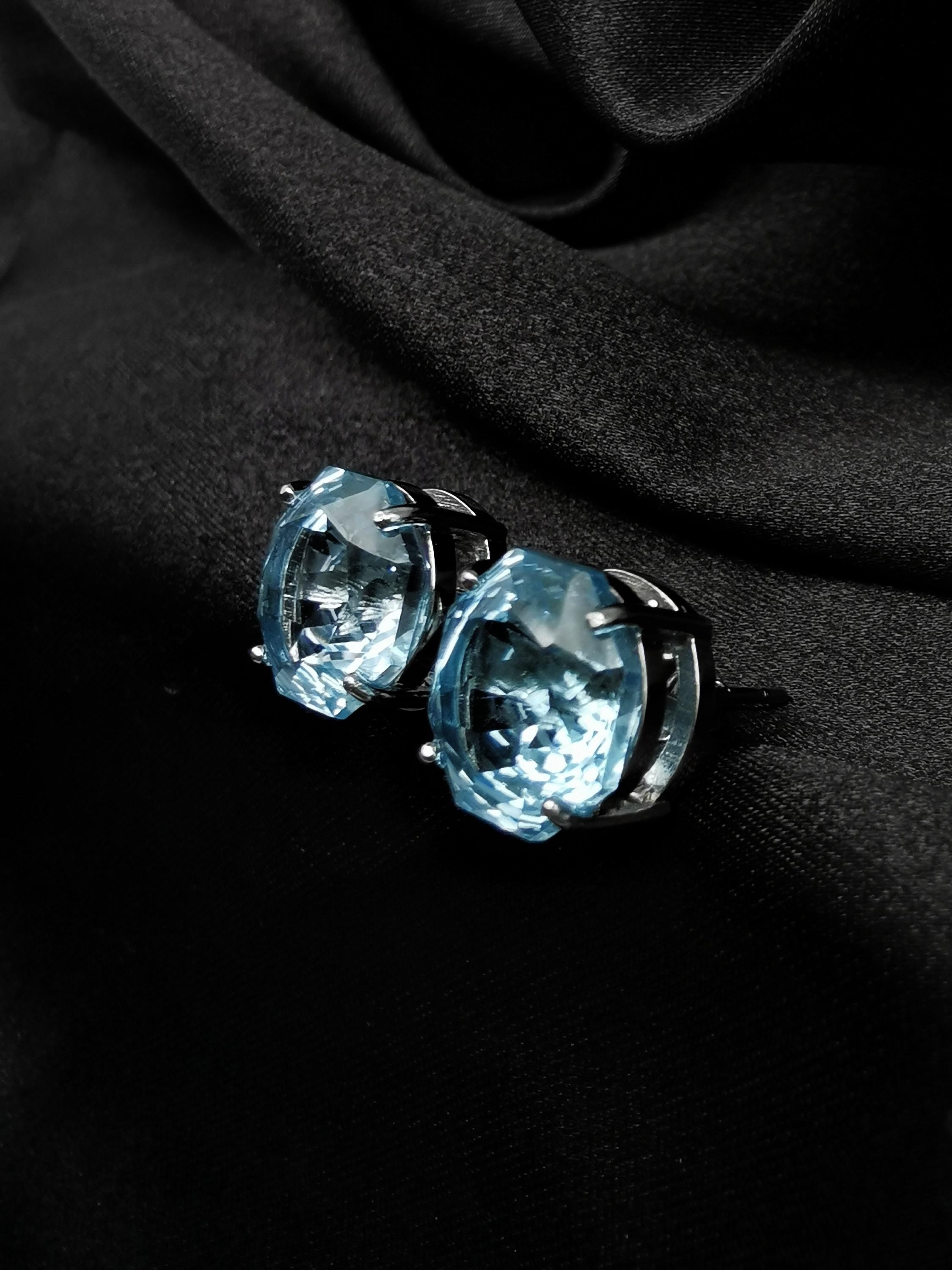 Blue topaz stud earrings close-up, faceted round stones with dark metal accents
