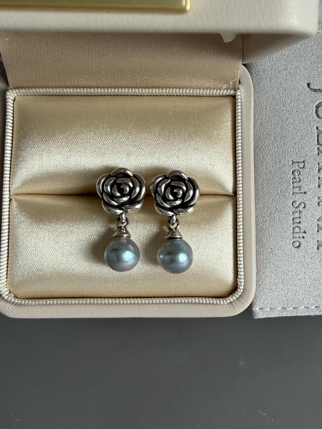 Silver rose earrings with pearl drops resting in the box insert