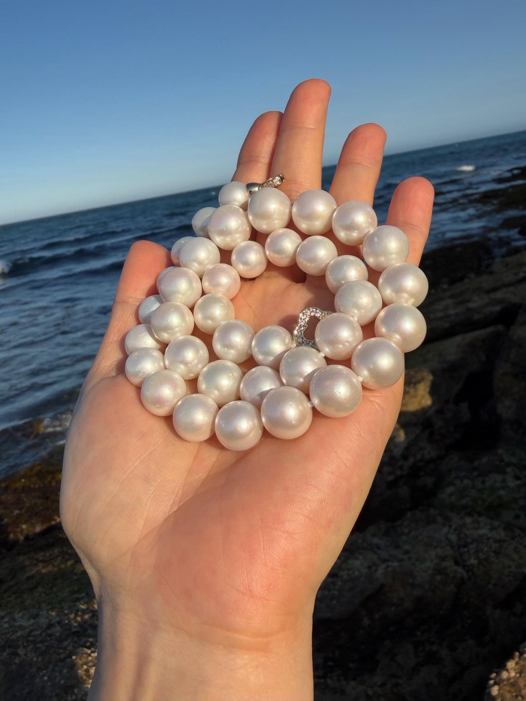 Pearl necklace with round iridescent pearls, held in front of the sea