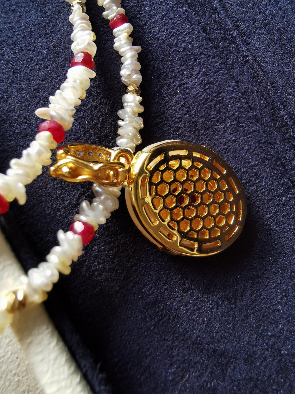 Gold oval pendant side with honeycomb texture and red center, with bead strand