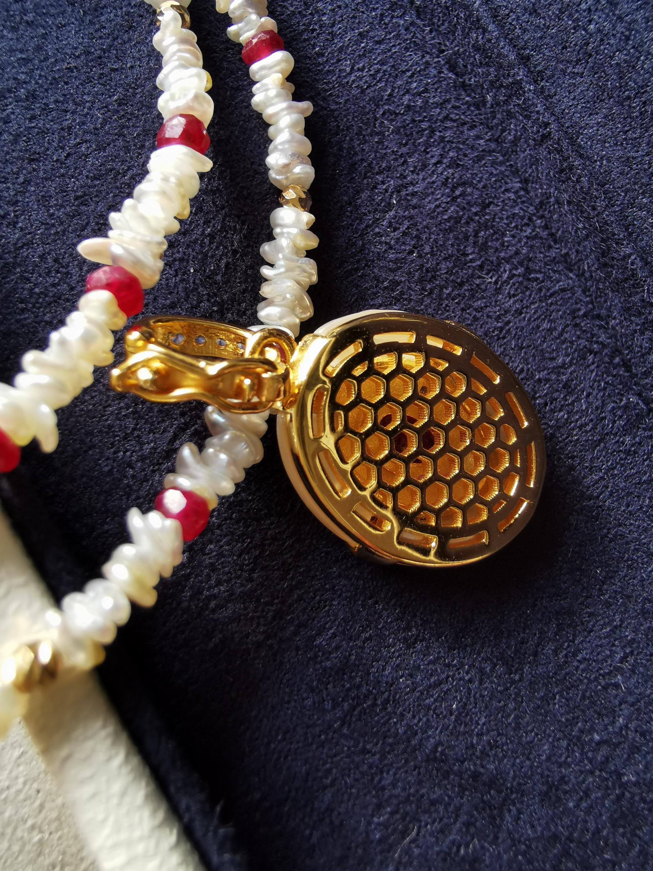 Gold oval pendant side with honeycomb texture and red center, with bead strand