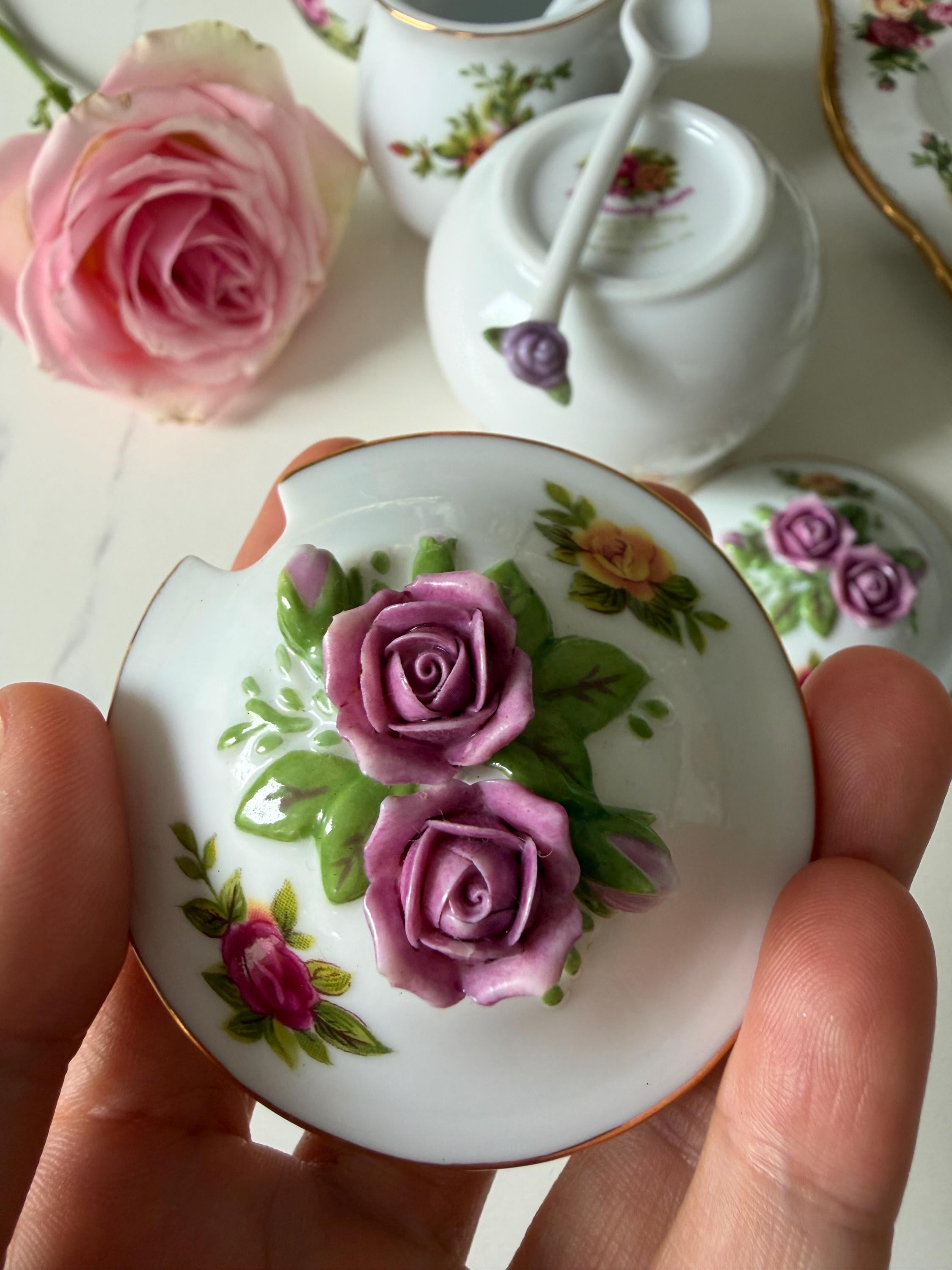 Porcelain sugar jar lid held in hand with purple rose and green leaf decoration