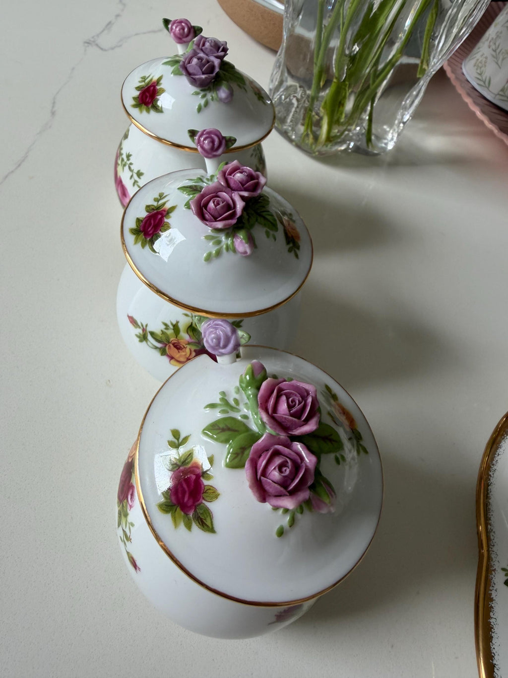 Porcelain jars with rose floral lids arranged in a vertical row with gold rim